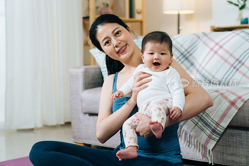 快乐的妈妈和宝宝对着镜头微笑。身穿瑜伽服的亚洲妇女正抱着她可爱的孩子拍照。