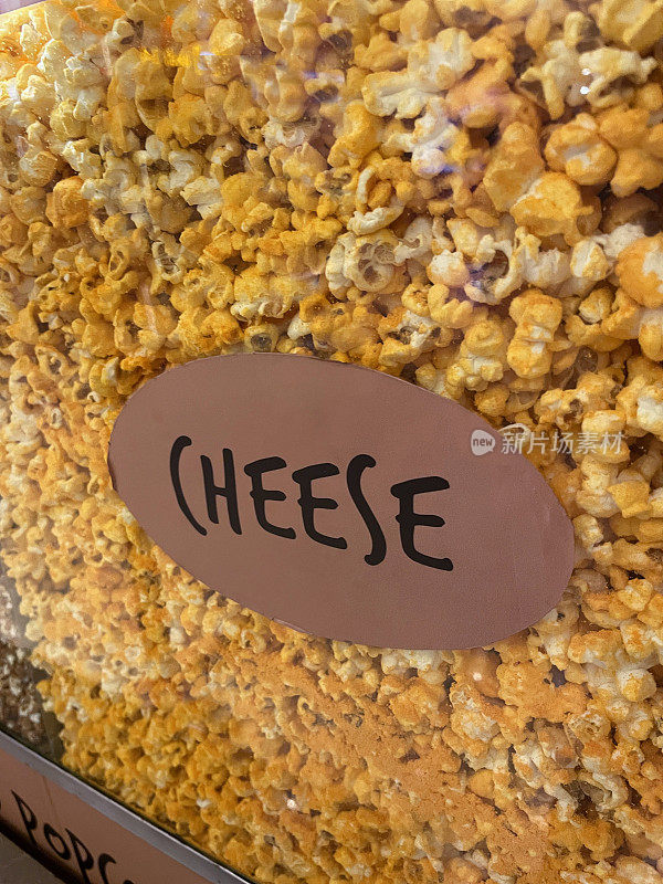 全帧图像的玻璃窗口的爆米花机标有奶酪和充满了温暖的爆米花裹在奶酪粉，影院零食的爆米花，重点放在前景