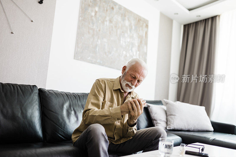 一名老人坐在家里的沙发上，患有关节炎，双手不舒服地搓着。老年人和健康问题的概念，手部疼痛可能是腕管的症状