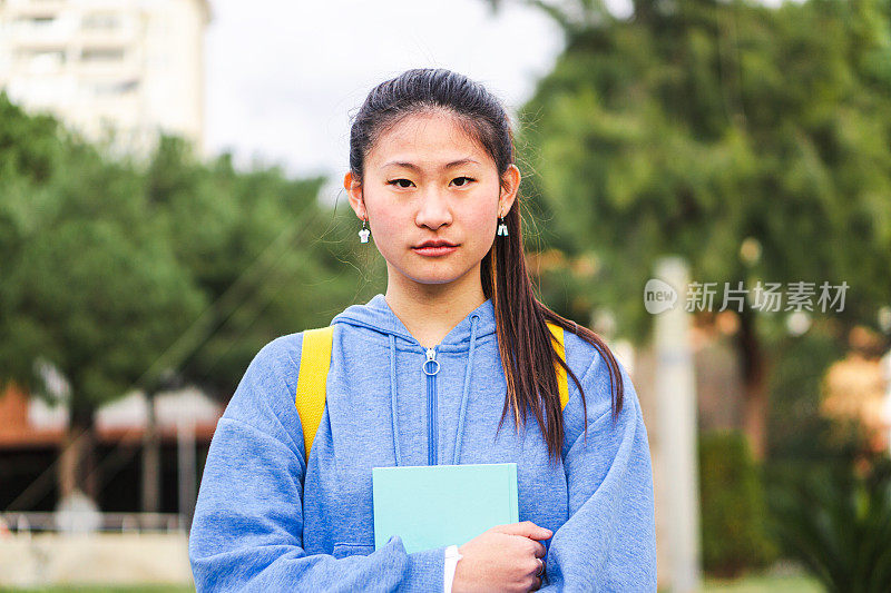 肖像严肃的青少年学生站在大学校园看着相机。年轻的中国女大学生。