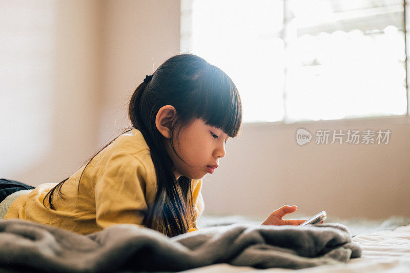 惊讶的女孩通过手机视频通话。女孩正躺在家里的床上。她正在度过闲暇时光。她在家很享受她的空闲时间。