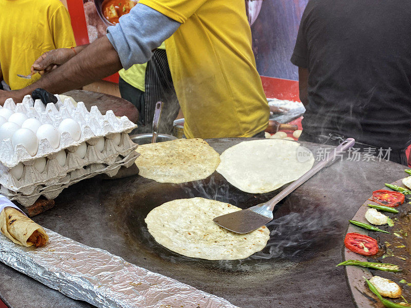 在塔瓦准备的街头食物的特写图像(大，扁平的金属烹饪锅)，油炸烤肉，食用油，金属锅铲，鸡蛋托盘，辣椒，高架视图，重点在前景