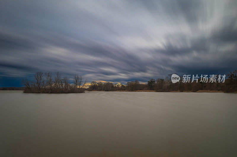 鸟岛在池塘中间。延时摄影。美丽的云被摄影技术模糊-使用ND滤镜。