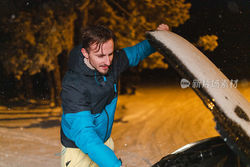 被困在雪地里的年轻人正在抬起汽车引擎盖