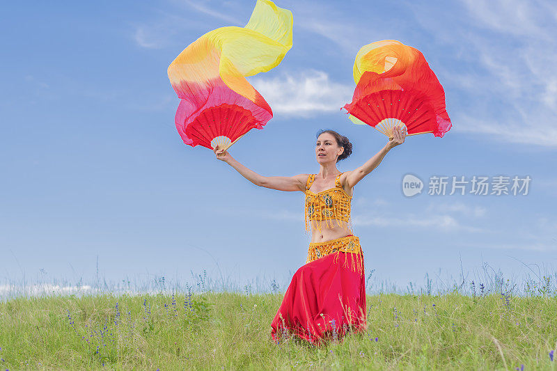 身着美丽东方服饰的女子手持扇子在蓝天下跳民族舞蹈