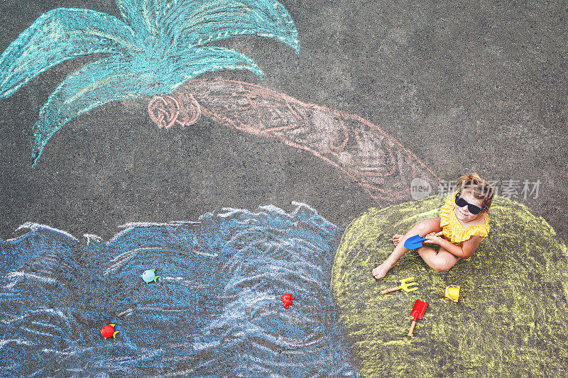 快乐的小学前班女孩在泳装充气环与海，沙子，手掌用彩色粉笔涂在沥青上。可爱的孩子与玩粉笔画的乐趣。夏天，假期，夏天