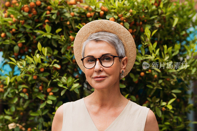 一个时尚成熟女人的肖像。白发苍苍的老妇人，戴着一副眼镜和一顶小草帽。