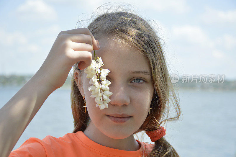 美丽的女孩拿着一朵白色的金合欢花，背景是蓝色的大海