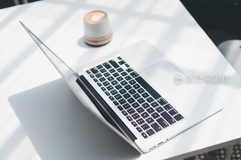 一杯拿铁咖啡和一台笔记本电脑放在咖啡店的白色桌子上