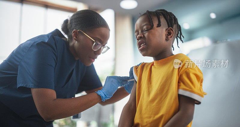 一个年轻的非裔美国男孩坐在光明医院的椅子上注射流感疫苗。黑人女护士正在打针。职业女性小心温柔，减轻痛苦