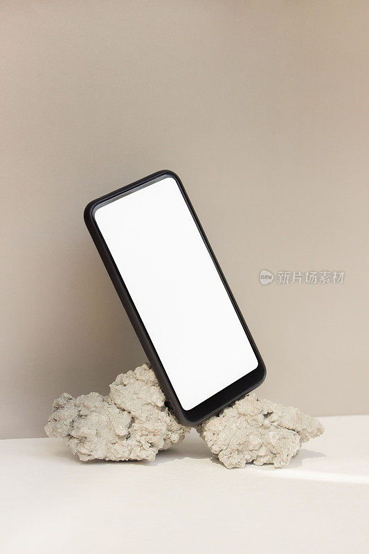原型模板智能手机平衡在米色背景上的天然石材。手机与空白屏幕模板