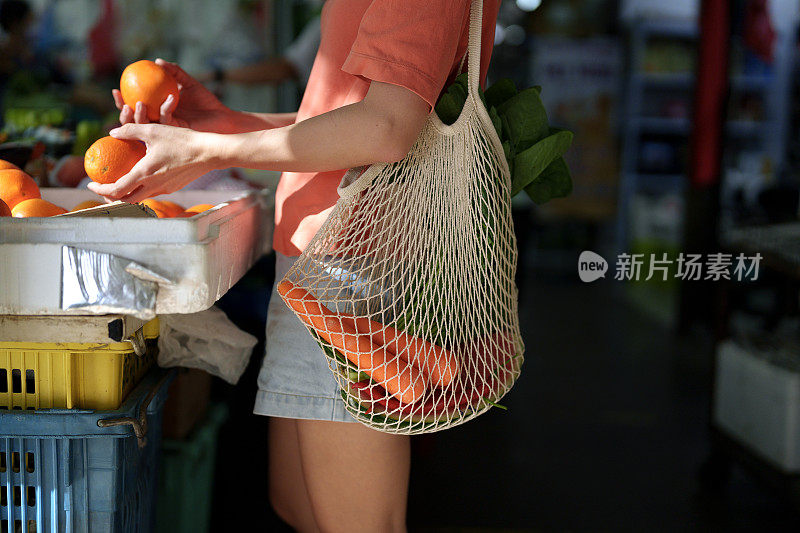 一名亚洲妇女在当地市场的摊位上购买新鲜蔬菜和水果时使用环保手提袋