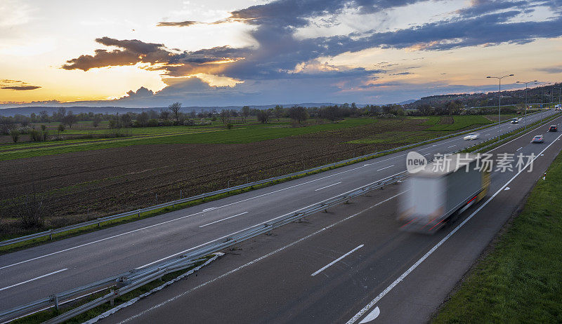 卡车在公路上高速行驶，穿过乡村风景。高速公路高速行驶。高速公路上超速行驶的景象。背景是美丽的日落。
