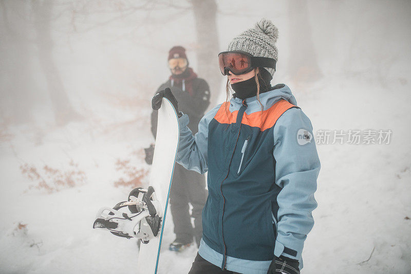 在一个雾蒙蒙的冬日，男女滑雪板运动员穿着冬装站在山上，准备滑雪