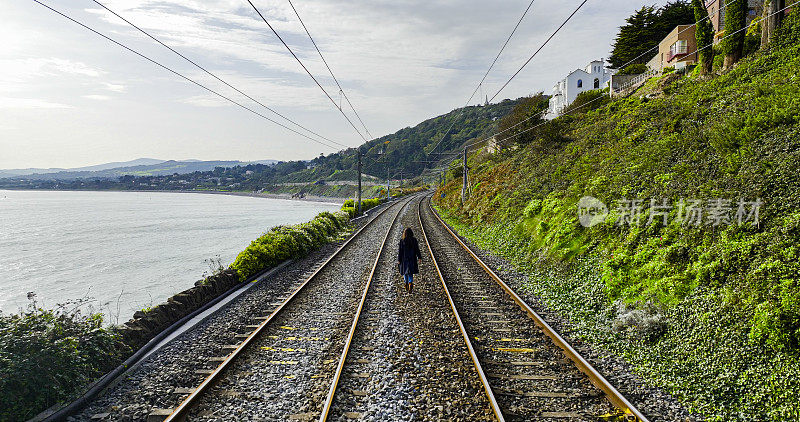 鸟瞰图:独自走在铁轨上的女人，走在铁路上的黑衣梦幻女人，独自行走的冒险