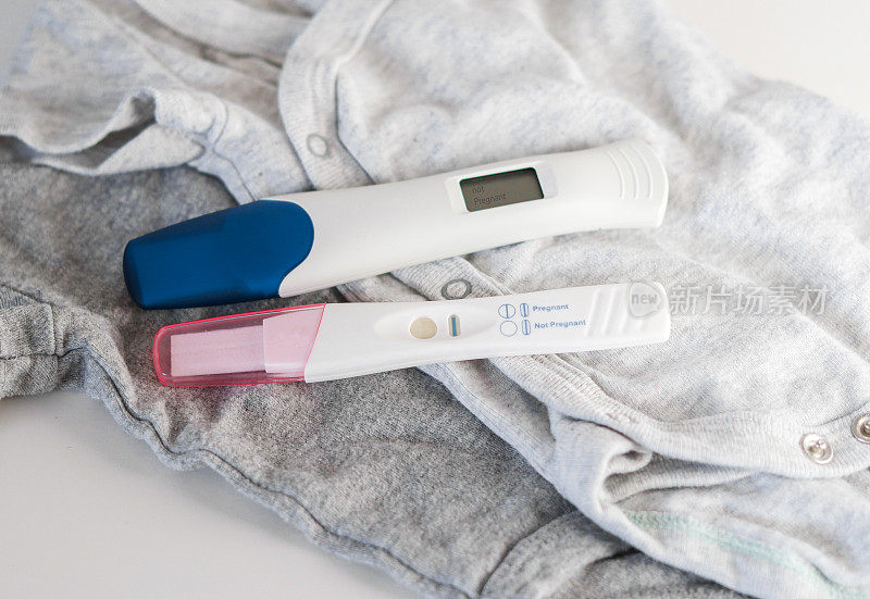 婴儿衣服上的两个阳性妊娠试验的俯视图