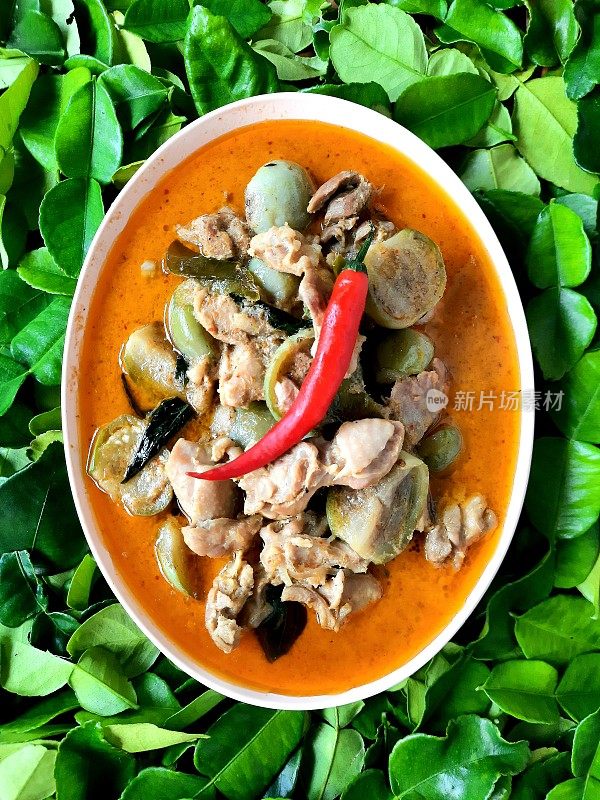 红鸡咖喱汤碗-佛手柑叶背景。