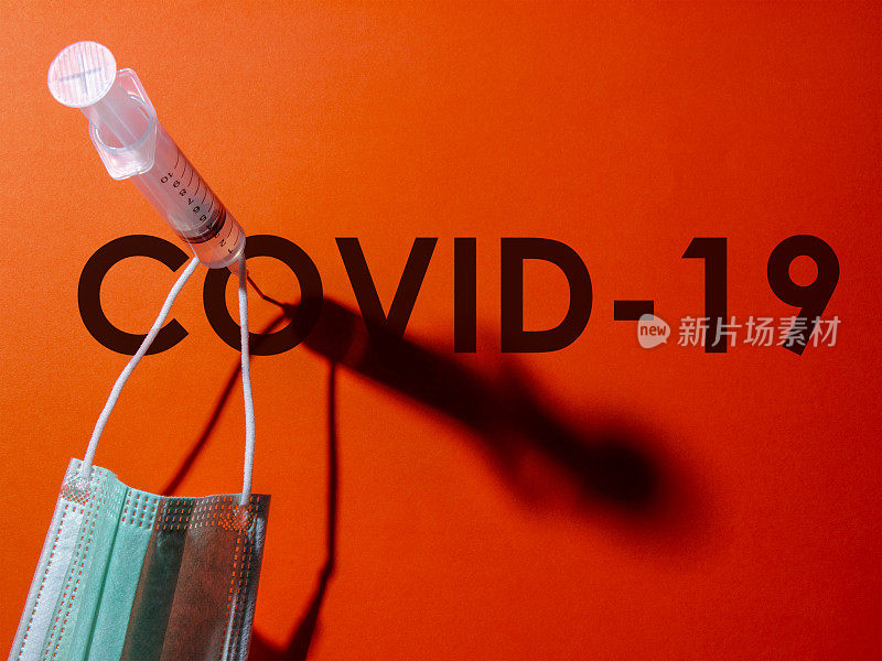 注射器上的针头穿过“COVID-19”单词“o”的中心，防护口罩挂在注射器上。