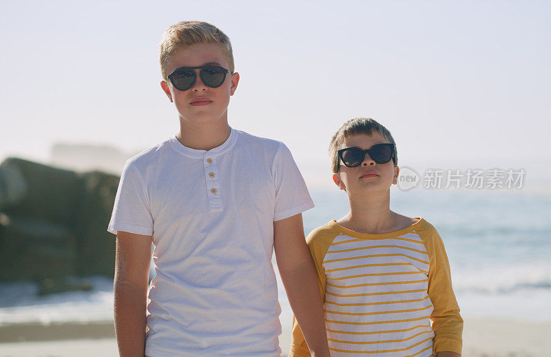 两个戴着墨镜站在沙滩上的年轻兄弟的裁剪照片