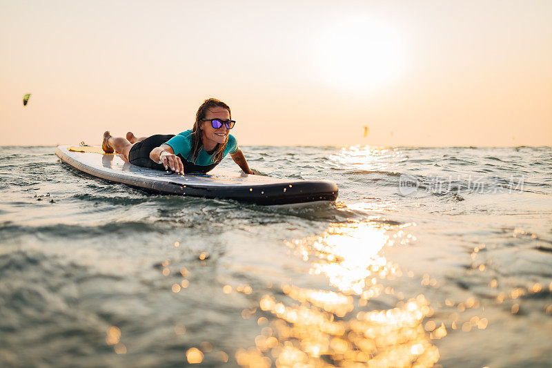 快乐的千禧一代妇女躺在海上的SUP板，今天开始她的冲浪冒险。