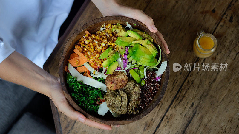 俯视图的女性手桌子设置，持有美味的健康素食碗豆腐，藜麦和鳄梨。为素食者提供健康多样的食物，包括大量的绿色蔬菜和新鲜蔬菜