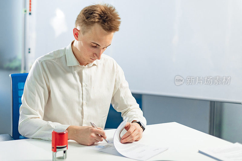 室内年轻商人的肖像。一名男子正在办公室签署协议和纸质文件