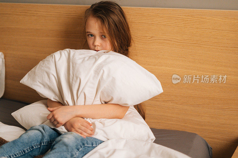 伤心的小女孩哭着独自坐在胎儿的位置，在床上摇晃着，抱着大枕头，看着相机。
