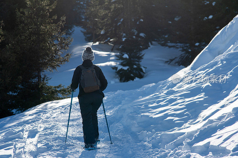 一名女子头戴羊毛帽，脚穿雪鞋，走在雪地上