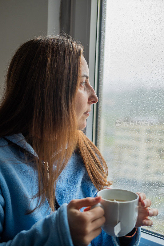 窗外下着雨，女人在窗前喝茶