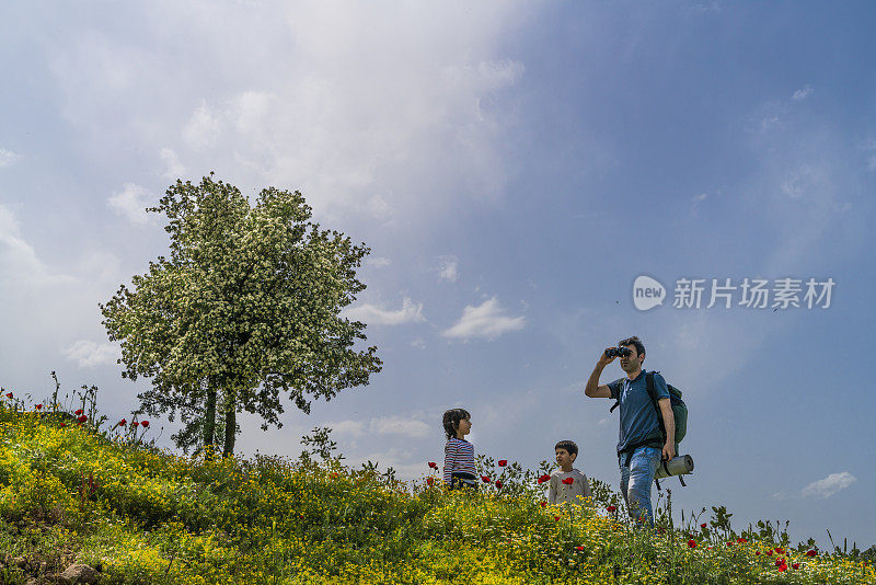 在野花和山楂树的春天景观中，背包客和他的两个儿子都在场。