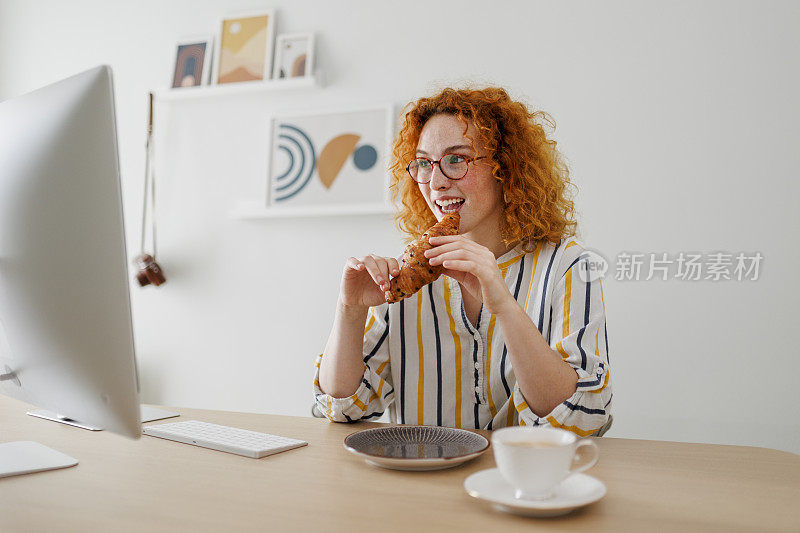 女人在办公室工作时吃牛角面包