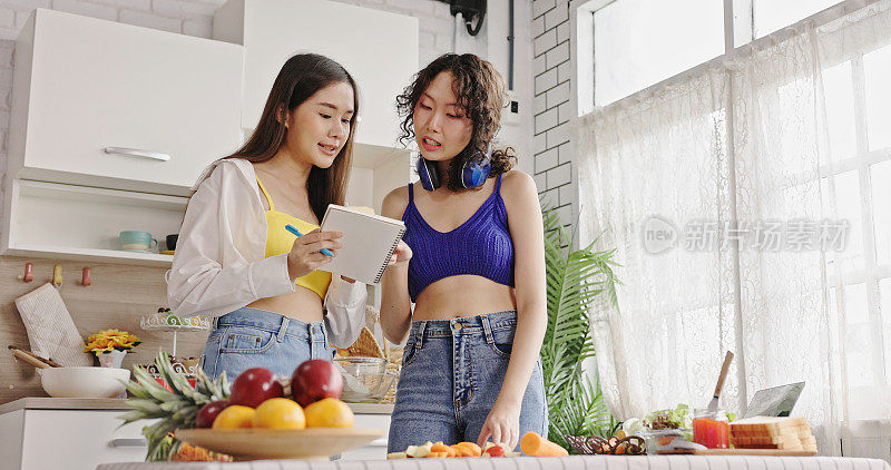 一名亚洲少女戴着耳机听着音乐，用水果刀和朋友们在厨房里做蔬菜沙拉。快乐地生活在一起烹饪娱乐。生活中很少奢侈。