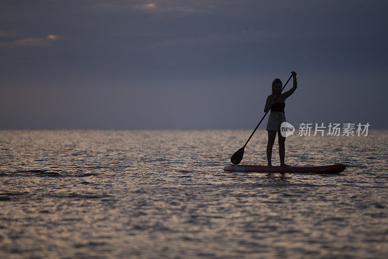 一位女性冲浪者在站立板上划桨。戏剧性的天空