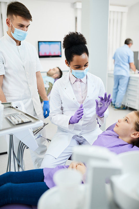 黑人女牙医在牙科诊所预约时与女孩交流。