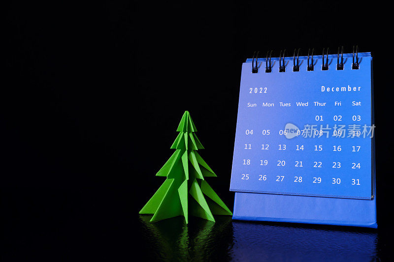 你好，2022年12月，圣诞概念。书桌日历与圣诞树上的黑色背景。