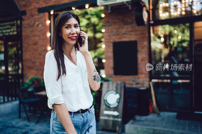 半身像，微笑的千禧女游客站在城市街道上，与最好的朋友进行国际智能手机通话，讨论旅行细节，漫游连接