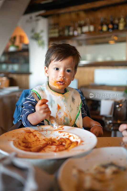可爱的蹒跚学步的孩子吃意大利面，把自己弄得非常脏，并享受它