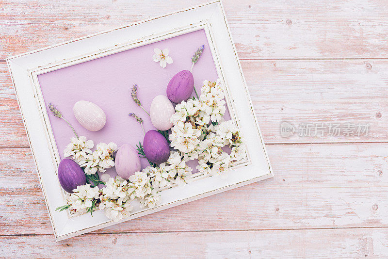 可爱的平面白色复古相框，淡紫色的表面，薰衣草茎，杏仁花和粉红色和紫色的复活节彩蛋。复古木制背景上的静物