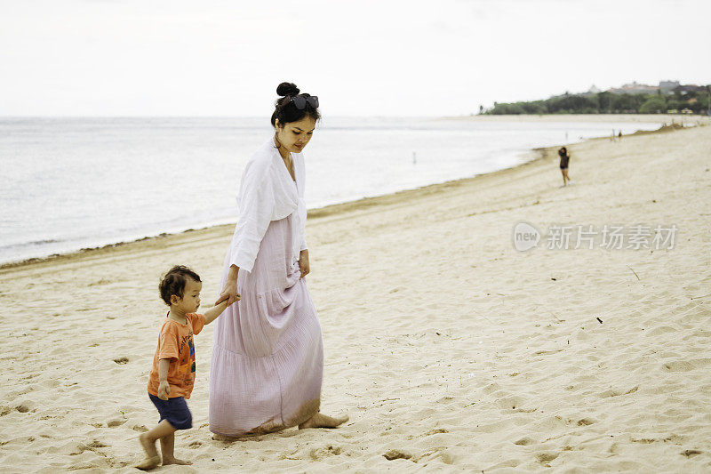 年轻的亚洲妇女在沙滩上教她的孩子走路