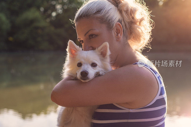 日落时分，在湖边与宠物狗共度时光的女人