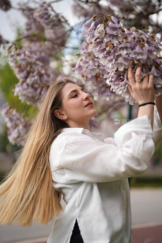 年轻女子在春天闻着树上盛开的花朵