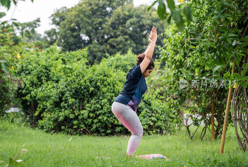 年轻的运动健康的妇女做瑜伽体式Utkatasana(椅子姿势)在公园户外