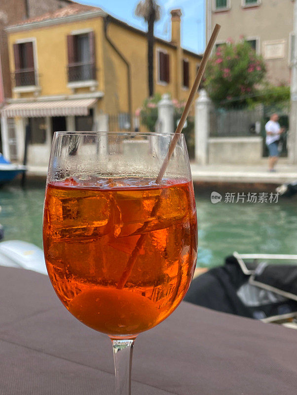 斯普利茨威尼斯鸡尾酒在玻璃装饰的橄榄木棒，普罗赛克，消化苦味，苏打水和冰块的特写图像，露天用餐设置，威尼斯运河的背景，重点在前景
