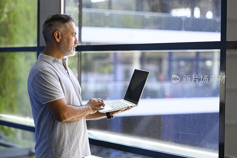 一个成熟的商人站在窗前用笔记本电脑工作