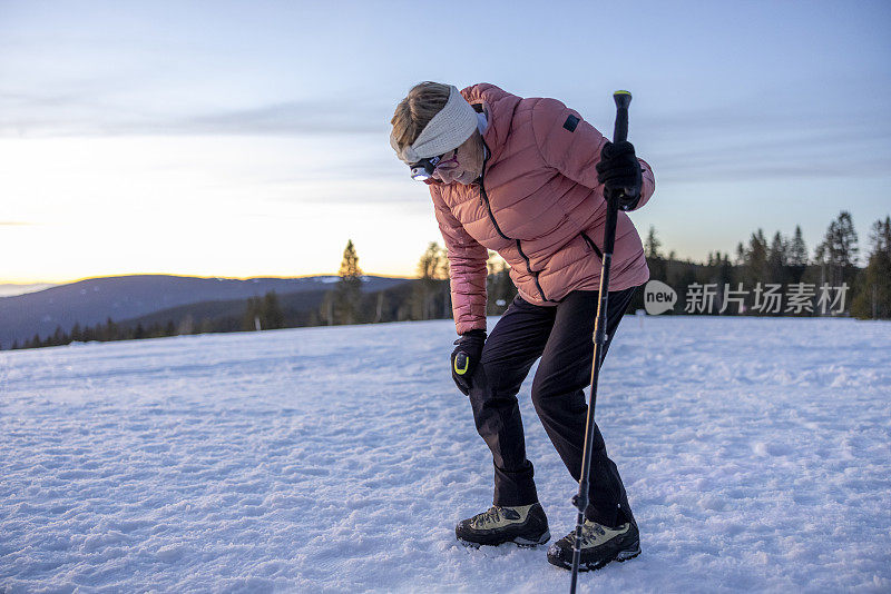 在雪山上徒步旅行的老妇人痛苦地抱着膝盖