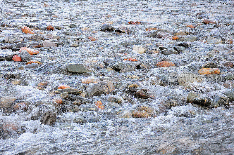 小圆石在湍急的小河中被秋日的余晖照亮。