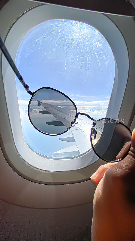 透过窗户看飞机带着太阳镜在机翼飞行与美丽的蓝天和岛屿。飞机窗外的景色。白天阳光明媚的白天。
