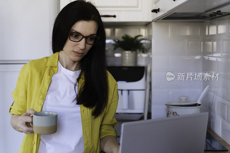 一个女人早上在厨房吃早餐时使用笔记本电脑。