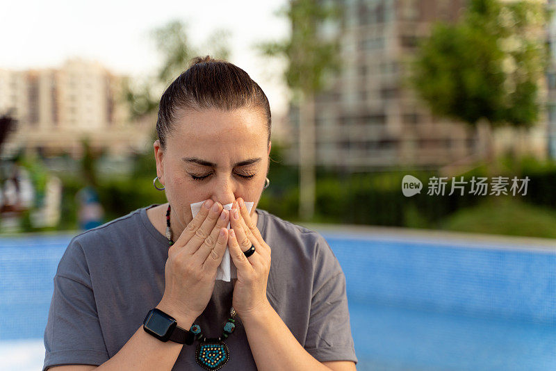 一名妇女在户外因过敏而打喷嚏