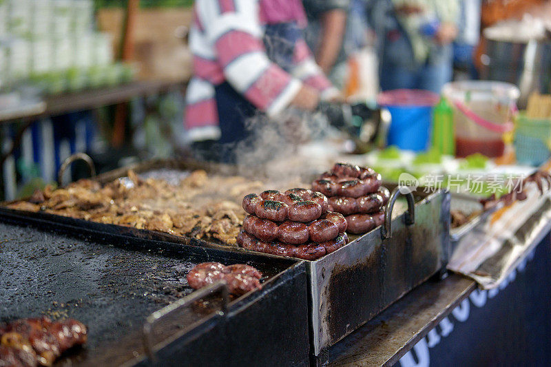 在一个特写镜头中，一个亚洲市场的小贩正在准备煎肉，展示了滋滋作响、美味可口的烹饪过程。